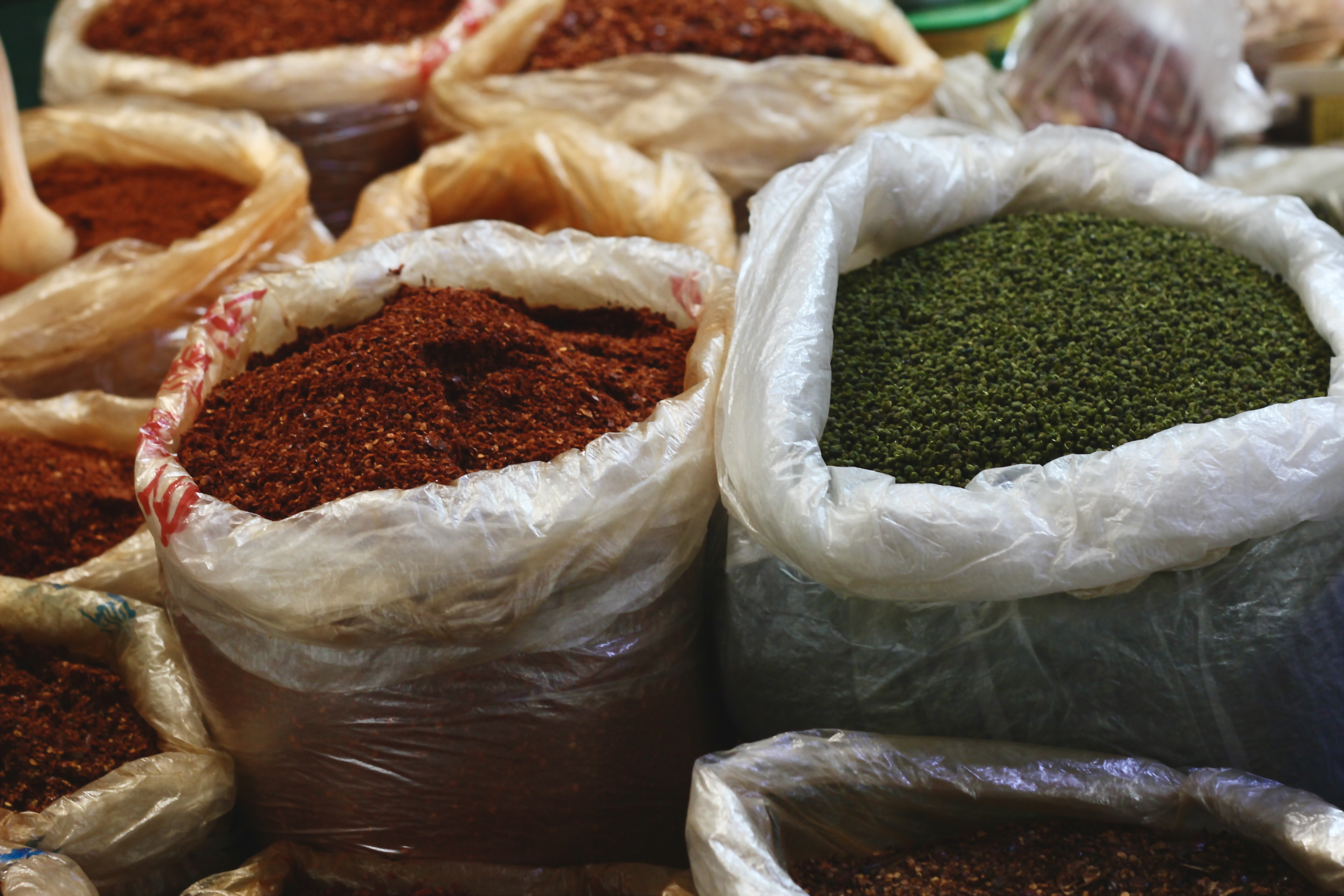 Large plastic bags filled to their brims with red and green chili peppers and pepper corns.
