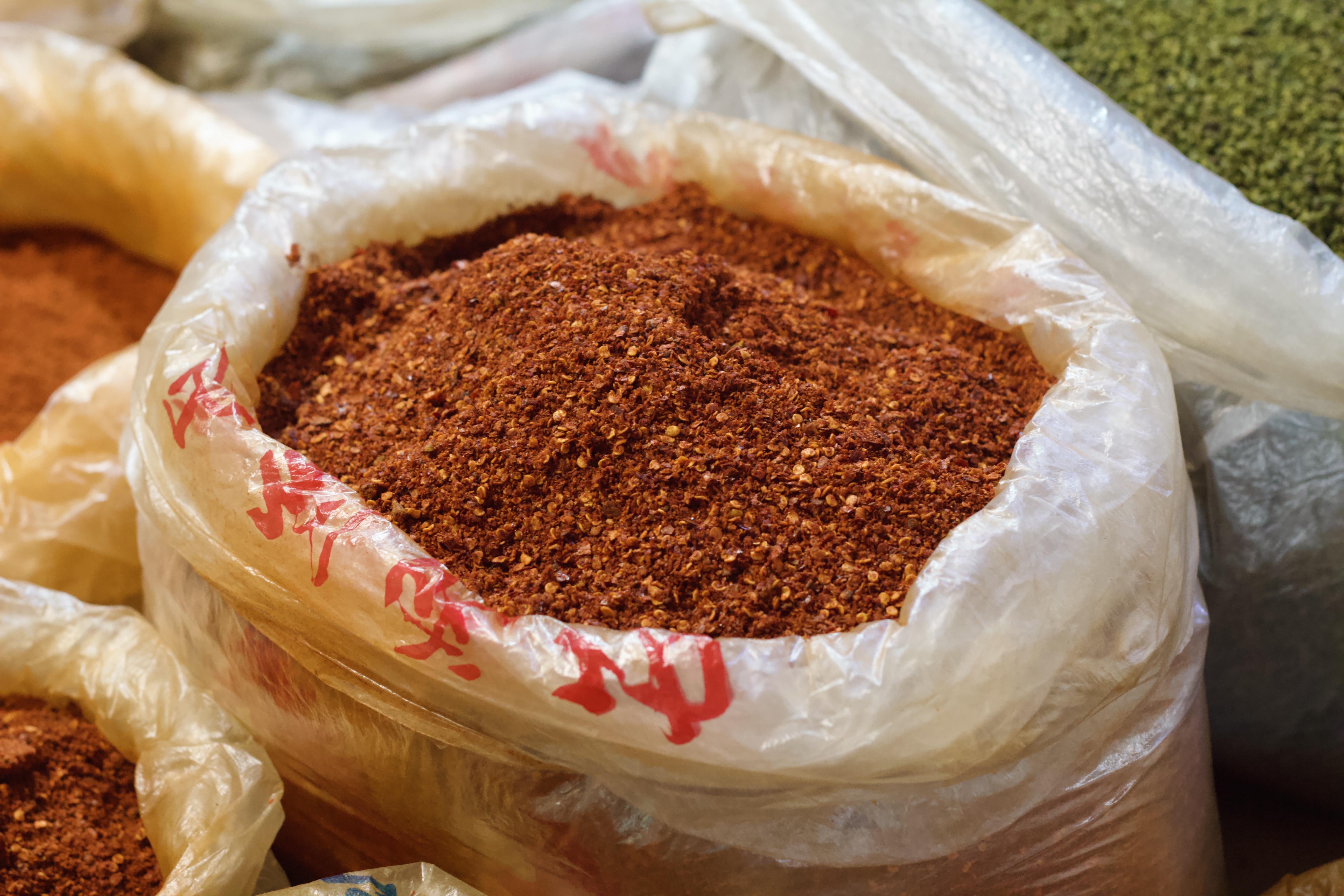 A large plastic bag filled to the brim with chili flakes, vibrant orange red.