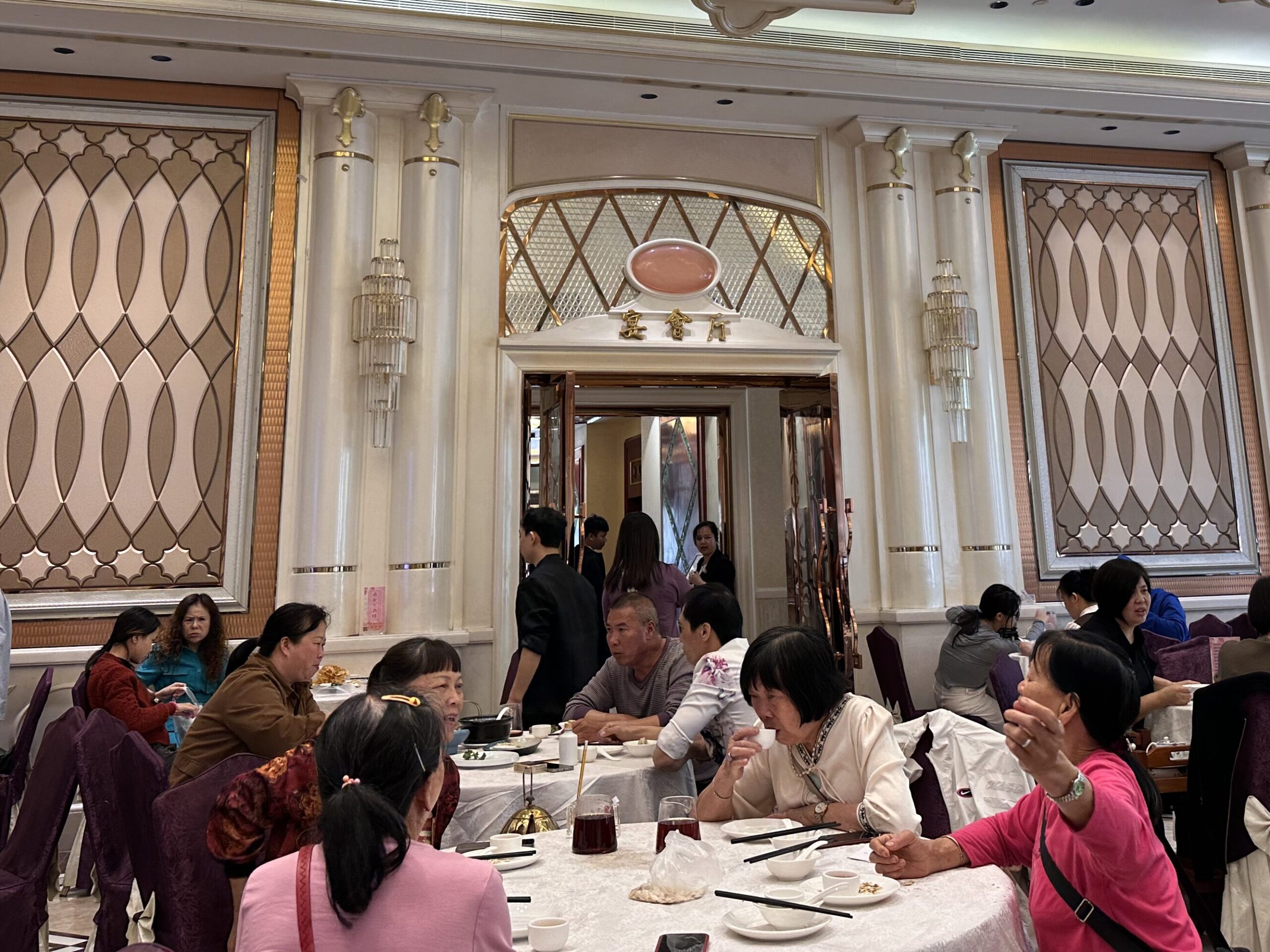 Cantonese people sitting in a banquet style hall at large round tables, enjoying various breakfast dishes and tea.