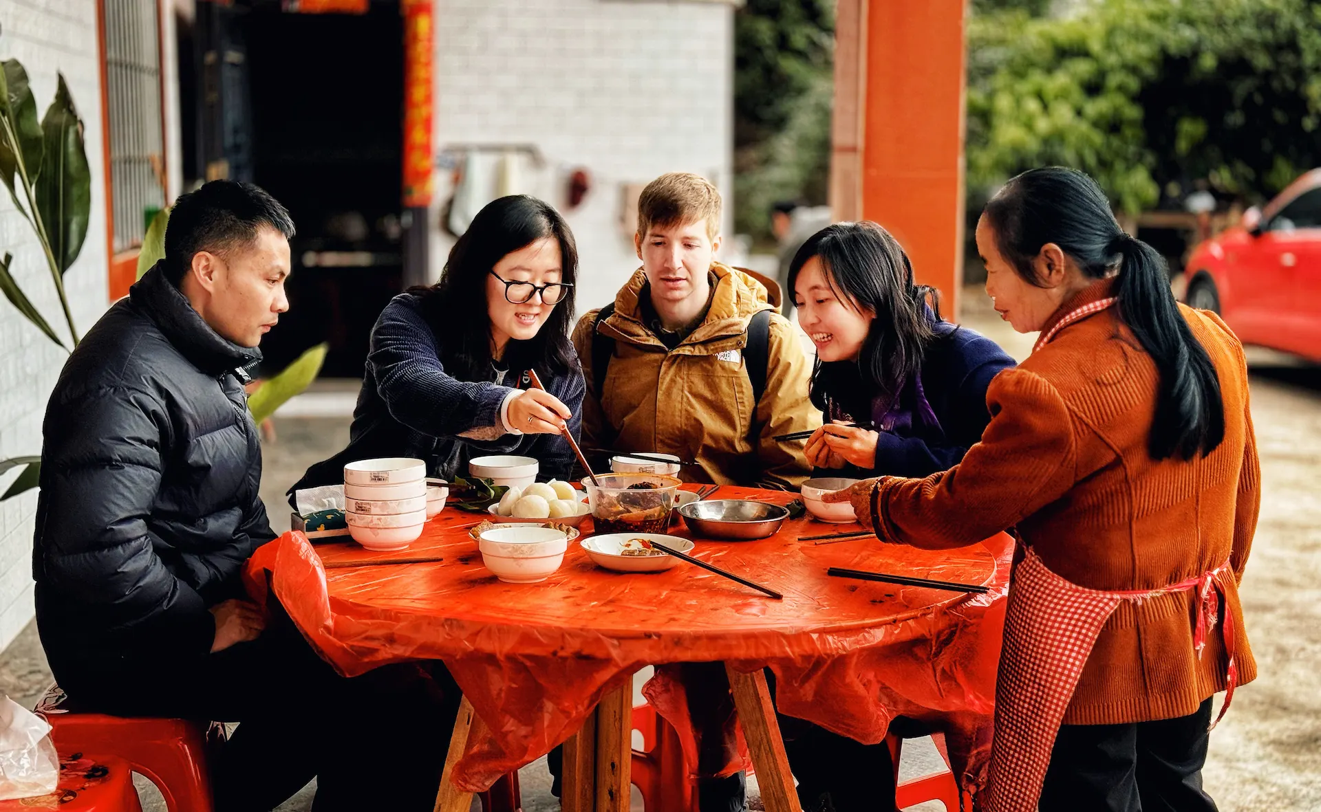 Five people crowded around a red table, tucking in to eat Huangba - a traditional rice treat in China