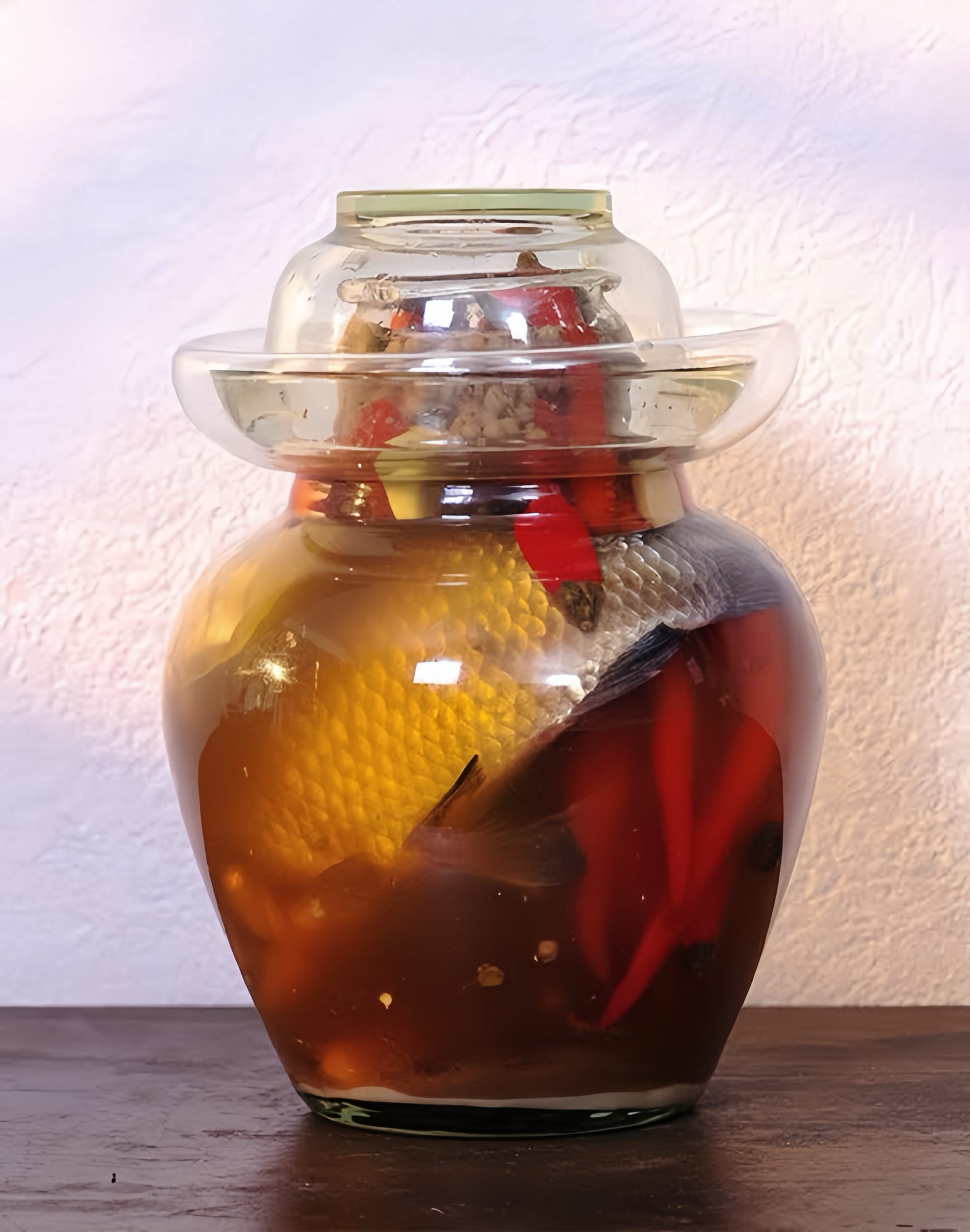 A glass Sichuan pickling jar full of whole chili peppers and a full fish.
