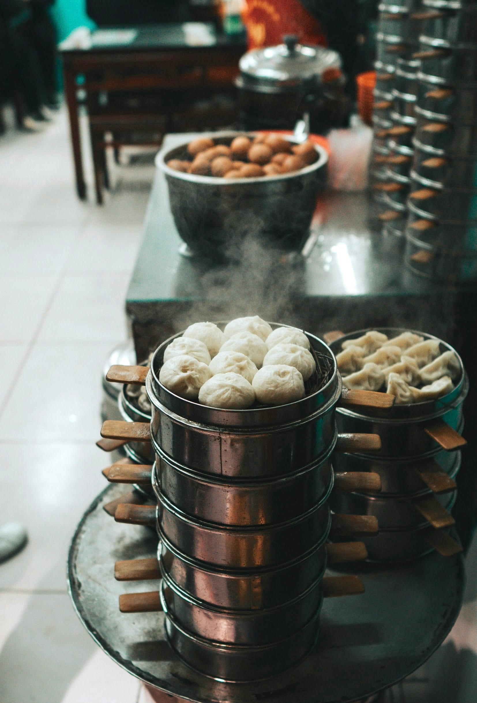 Kitchen steaming trays stacked one on top of the other on a table. One stack contains baozi, the other dumplings.