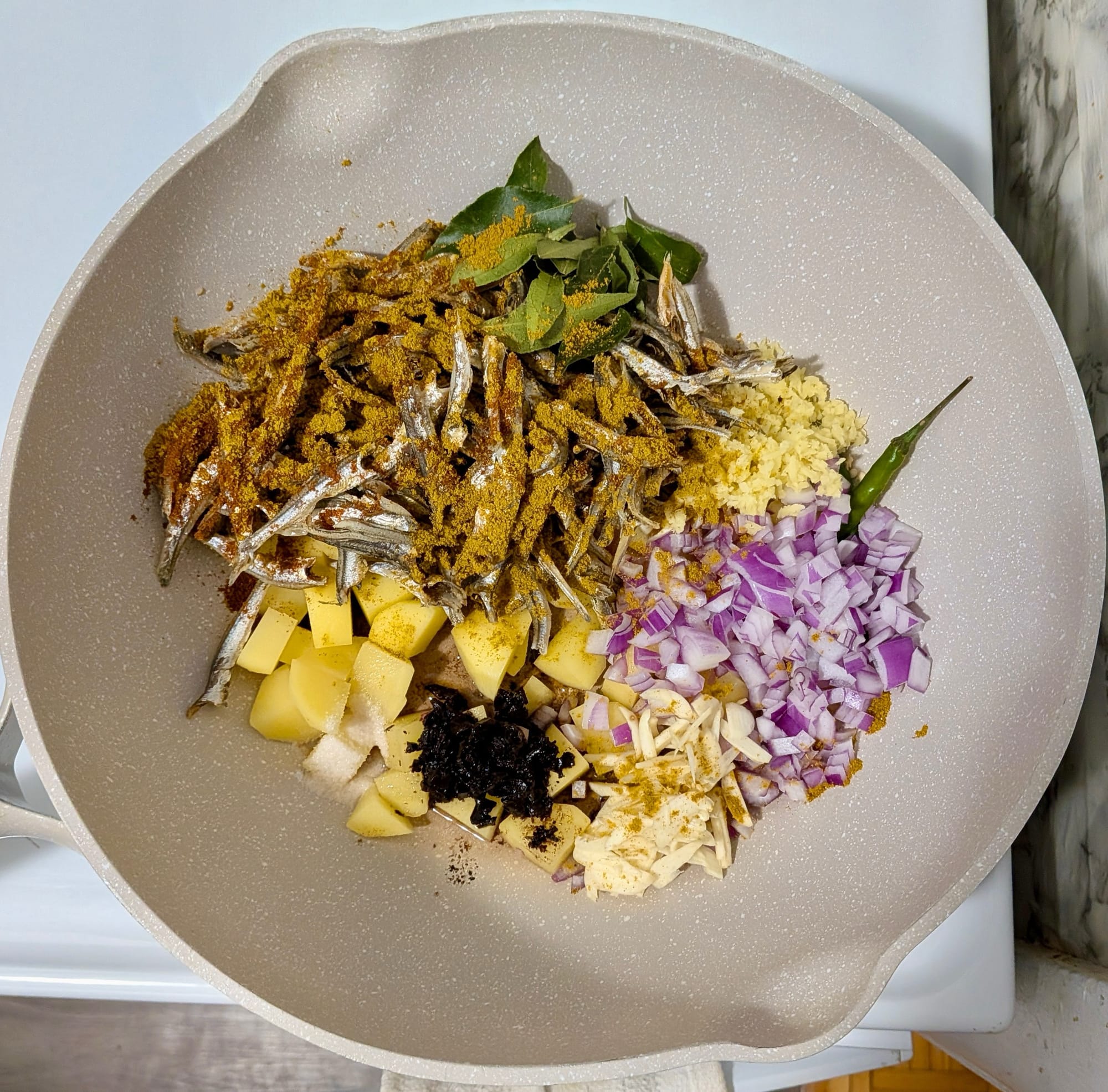 Diced red onions, potatoes, and various spices in a pot on a white stove.