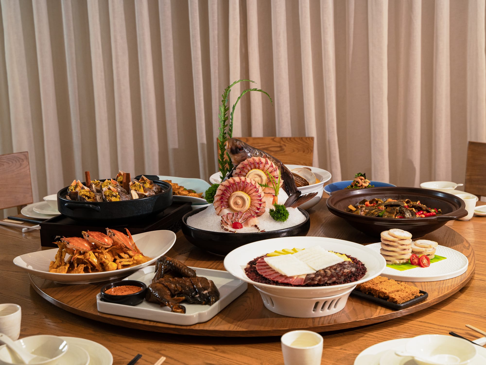 A large round table with a lazy susan in the center covered in various seafood dishes such as crabs, fish, and other assorted dishes.