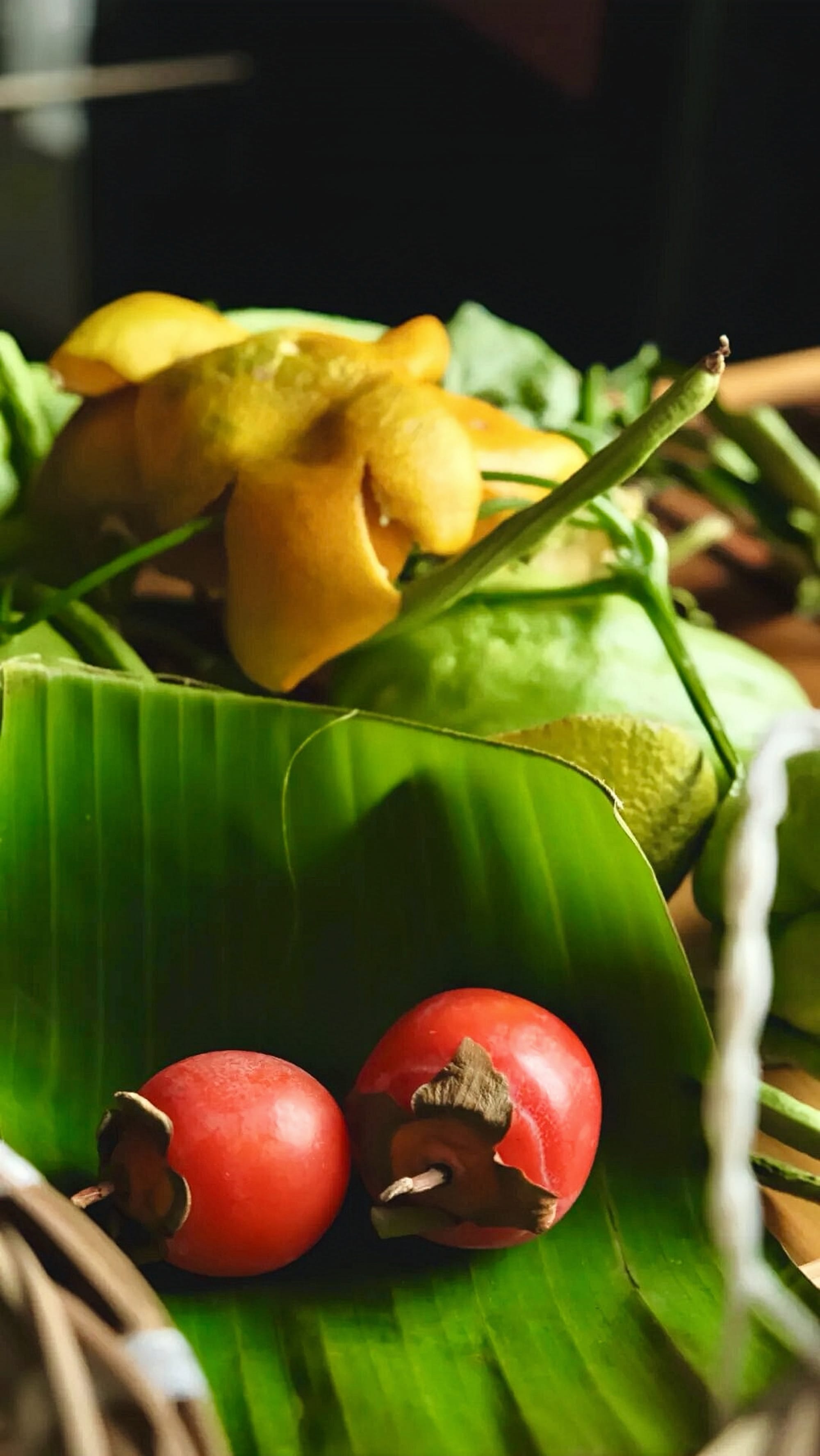 A big green leaf contains two small bright redish-orange persimmon fruits.