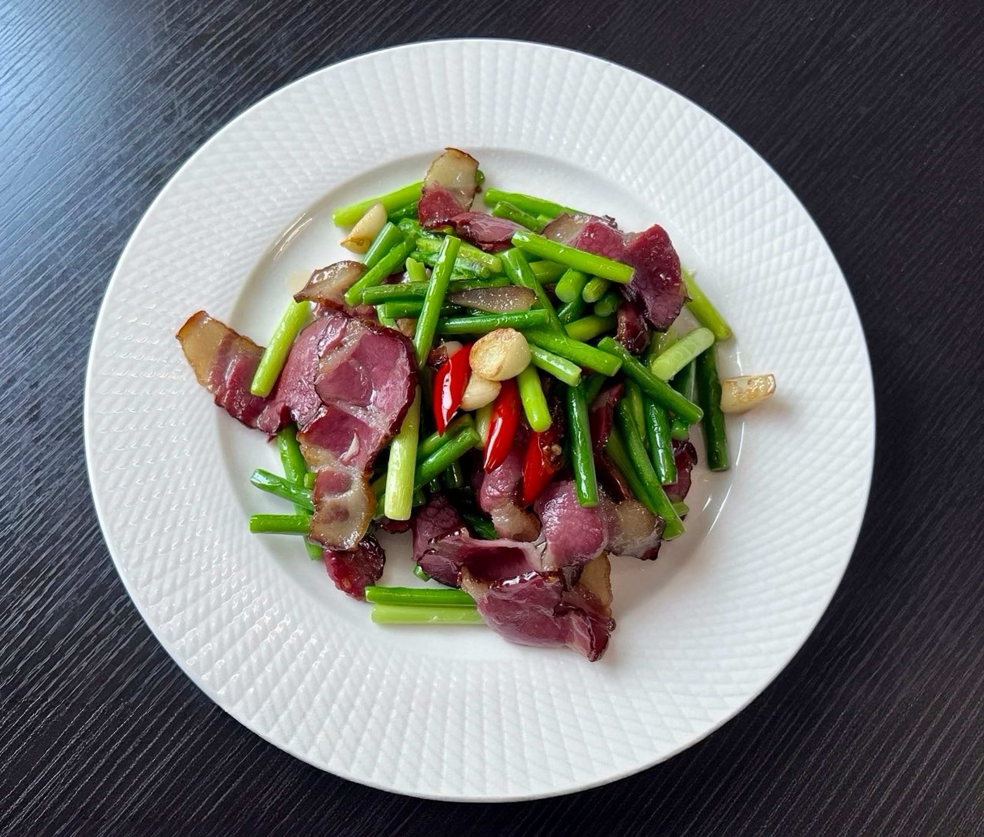 A white plate with stir-fried onion chutes, pork, garlic, and a diced red chili pepper