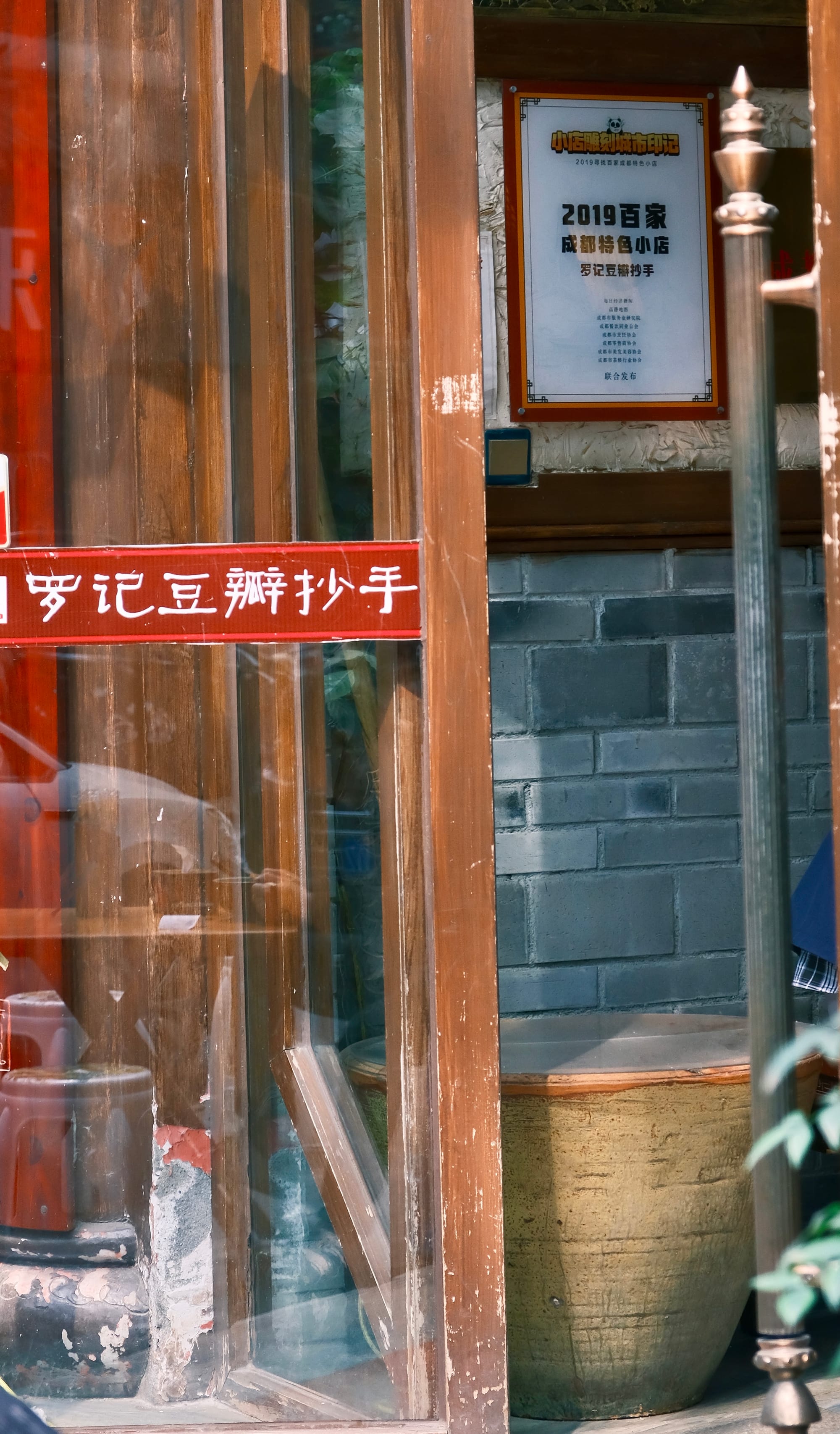 The door and entrance to Luo’s Doubanjiang Wontons. A simple entrance with a glass door and a clay urn set just inside the door on a traditional gray stone brick wall.