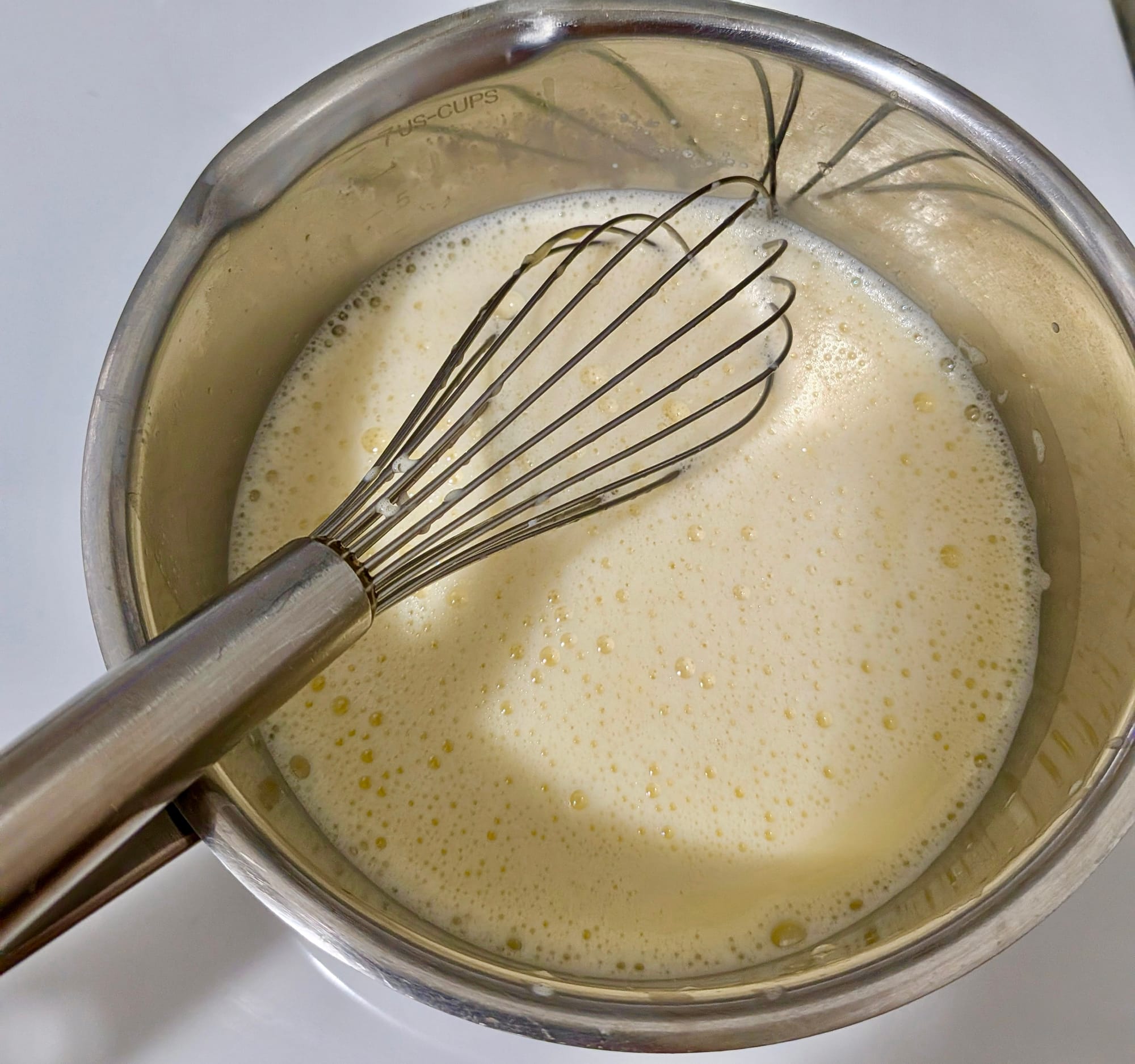 A pot with cream and a whisk, cooking on the stove.
