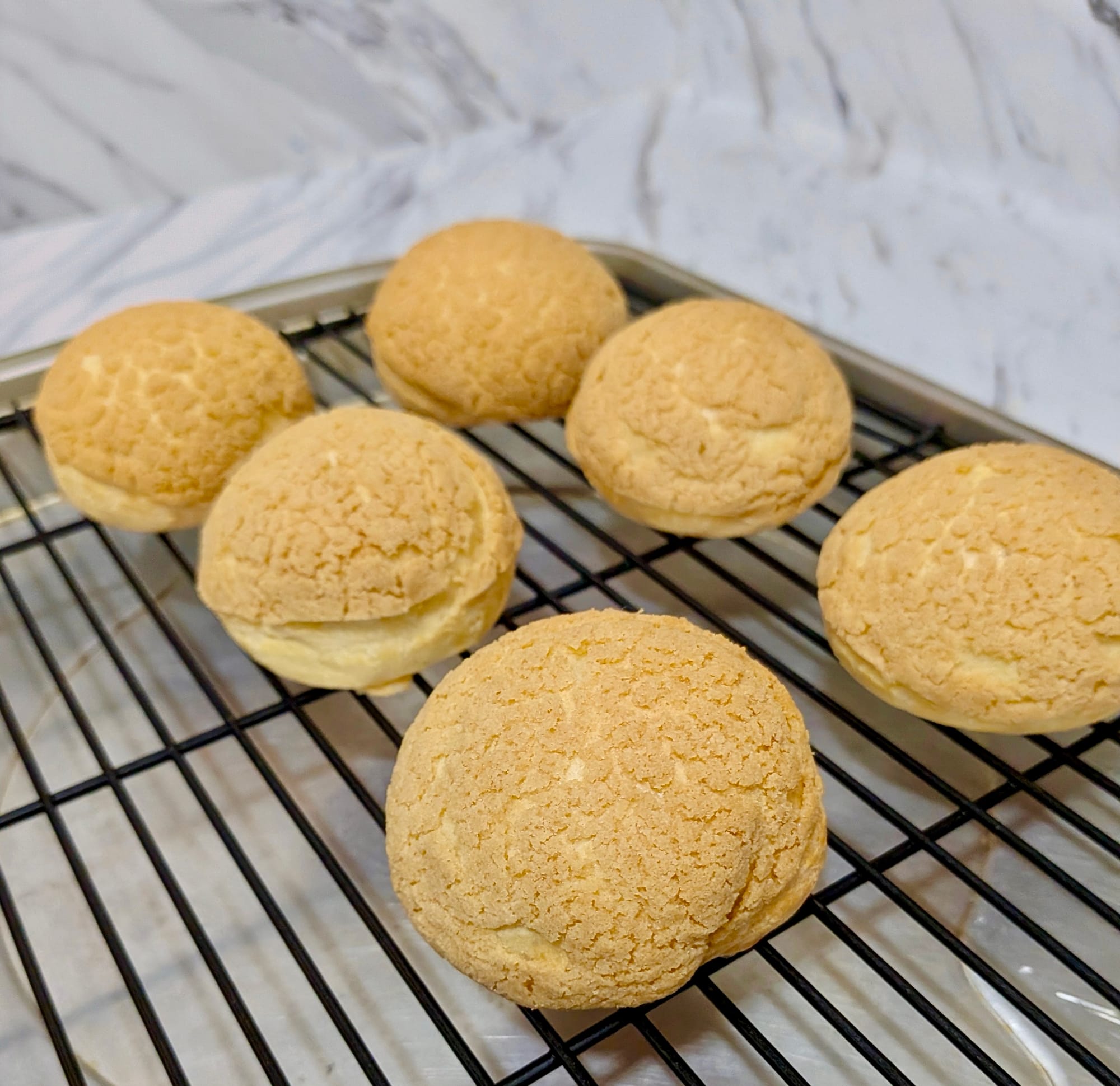 Six finished choux pastries on a cooking rack.
