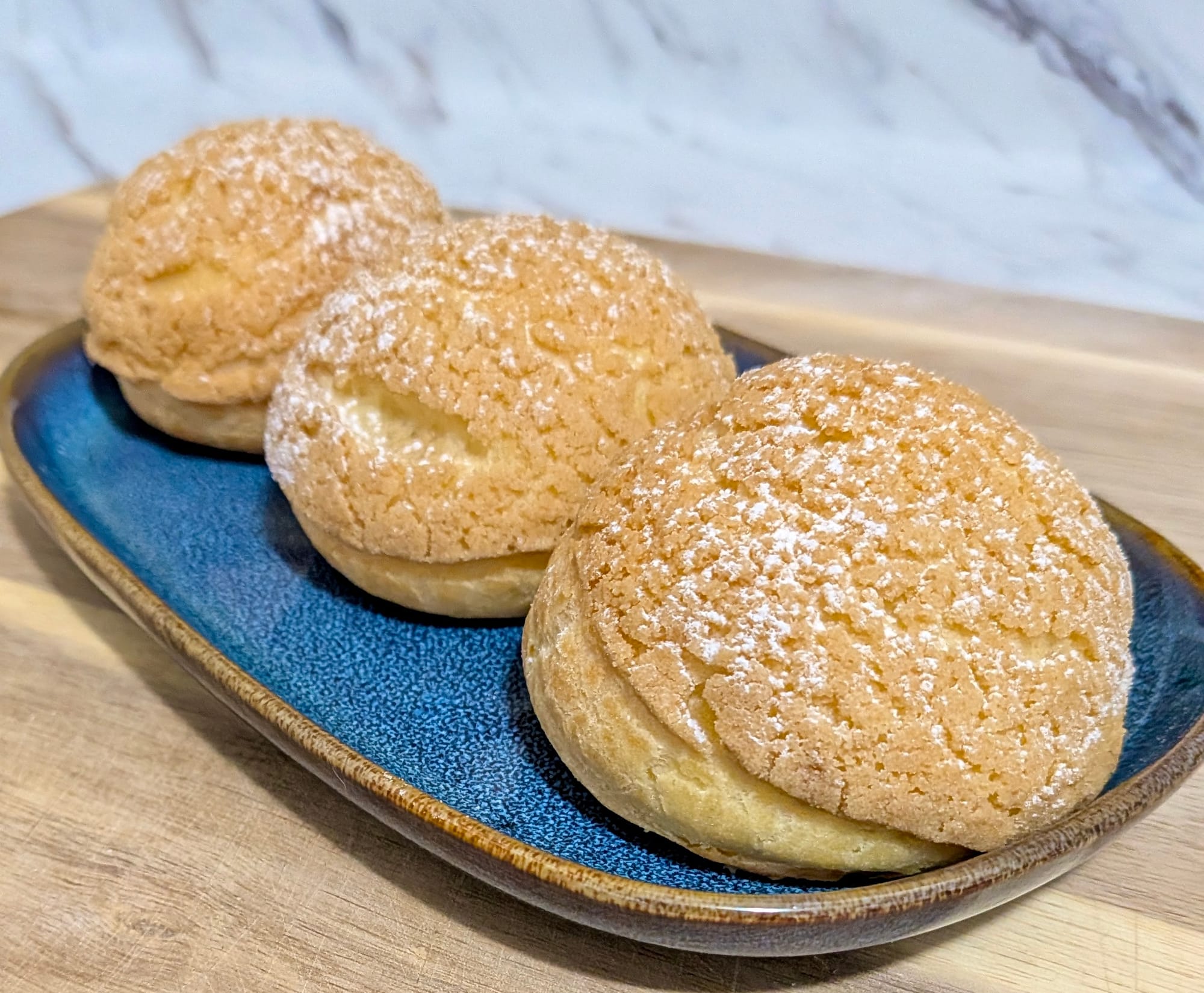 Three Lemongrass Petite Choux on a blue tray, lightly dusted with icing sugar.