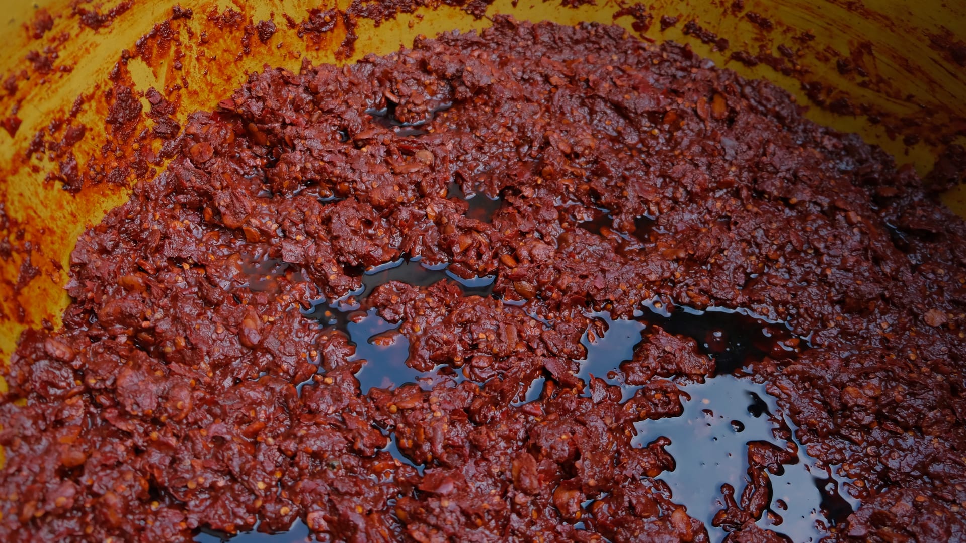 Doubanjiang, fermenting, close up in a pot. Liquid sits around moist, red broadbeans.