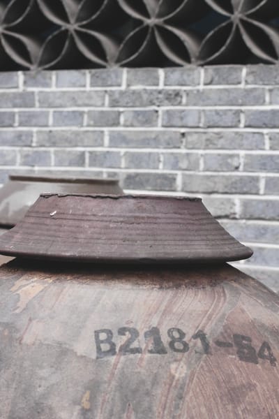 The top of a brown weather-worn ceramic vinegar jar stamped with its vat number in black ink.