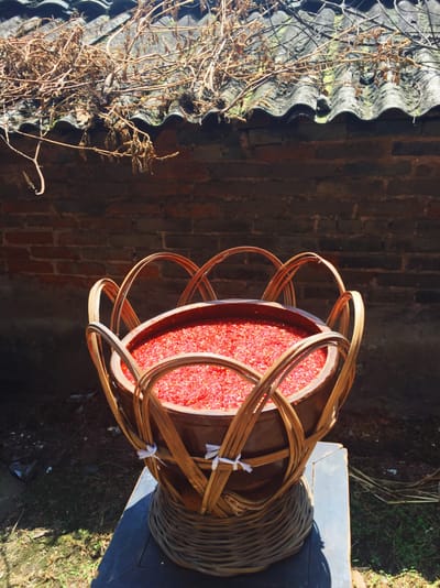 A large brown bamboo bowl filled with ground red chili peppers.