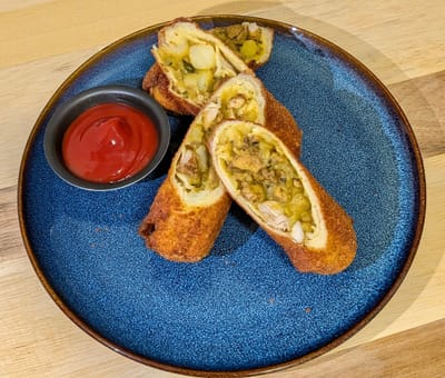 Plated chicken rolls sliced in half, leaning on each other with a dipping saucer of ketchup.