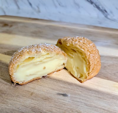 A single lemongrass petite choux sliced in half on a cutting board, showing the pale yellow creamy center.