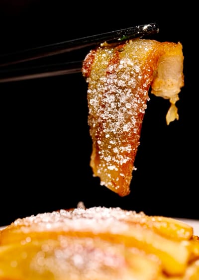 Chopsticks holding a piece of Jia Sha Rou - a piece of pork covered in granulated sugar.